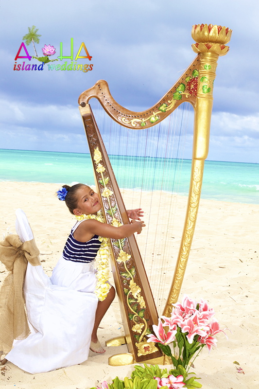 Little girl playing a golden harp on the beach with tropical flowers